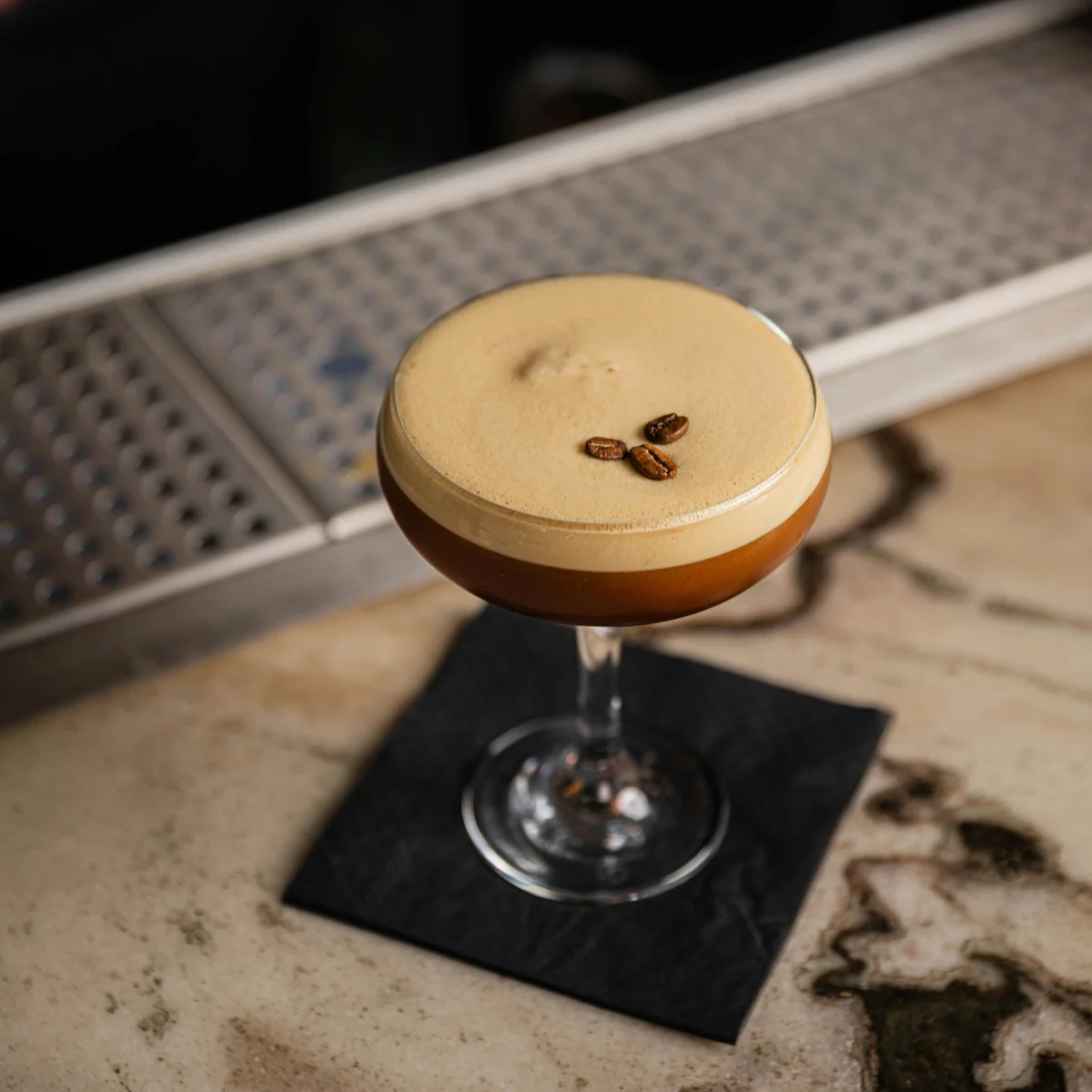 Ly cocktail Espresso Martini với lớp bọt crema nâu nhạt và ba hạt cà phê