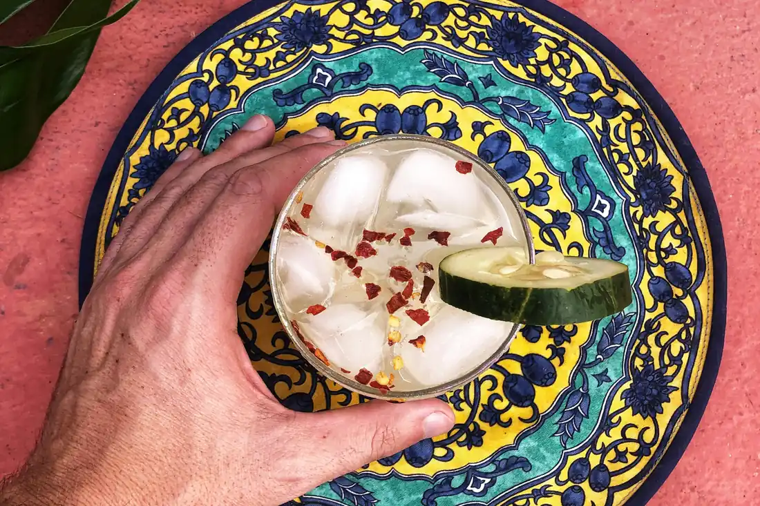 Một ly mocktail có đá, dưa chuột và ớt khô, đặt trên đĩa gốm hoạ tiết