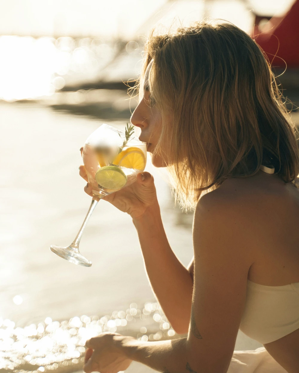 Người uống đưa ly cocktail có lát chanh vàng và chanh xanh lên sát mũi trước khi nhấp