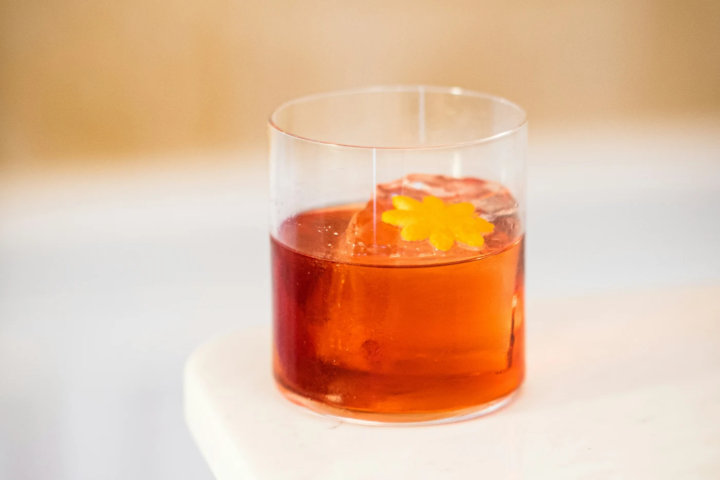Ly Negroni màu đỏ ngọc với viên đá to và vỏ cam xoắn, đặt trên mặt bàn đá