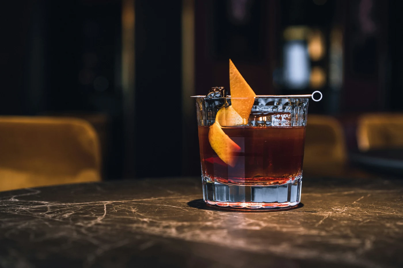 Ly Old Fashioned với một viên đá to và vỏ cam vắt, đặt trên mặt bàn đá tại quầy bar