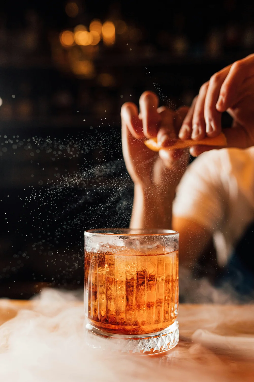 Bóp gập dải vỏ cam trên miệng ly Old Fashioned, tinh dầu bắn ra thành màn sương li ti