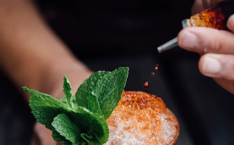 Nhỏ vài giọt bitters từ ống nhỏ giọt lên ly cocktail đá bào có bạc hà